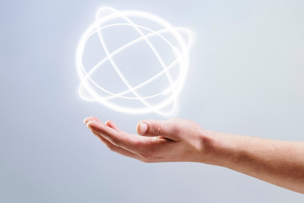 This image shows a human hand extended with an abstract glowing sphere hovering above it. The sphere consists of intersecting white neon-like lines, giving a futuristic and digital aesthetic. 